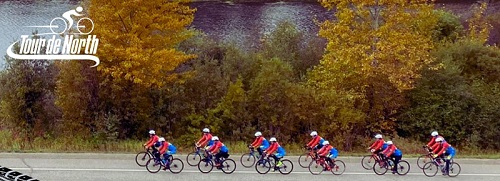 Tour de North logo on a fall backdrop with 12 cyclists riding from right to left