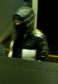 Suspect 02 entering the store. They are wearing a shiny black and white coat with the hood up. 