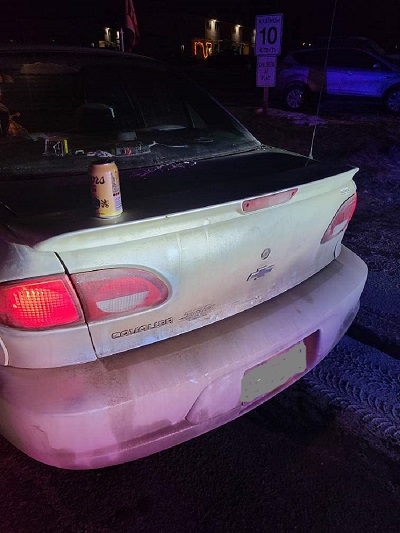 A night photo of the back end of a car with a can of Coors beer on the trunk 